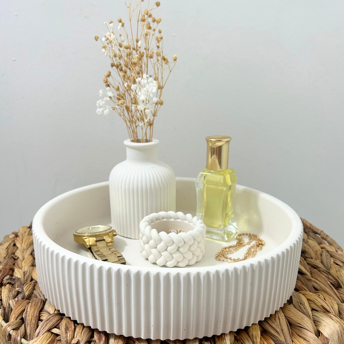 White jesmonite tray with decorative items including a vase, bottle, and jewelry on a woven mat.