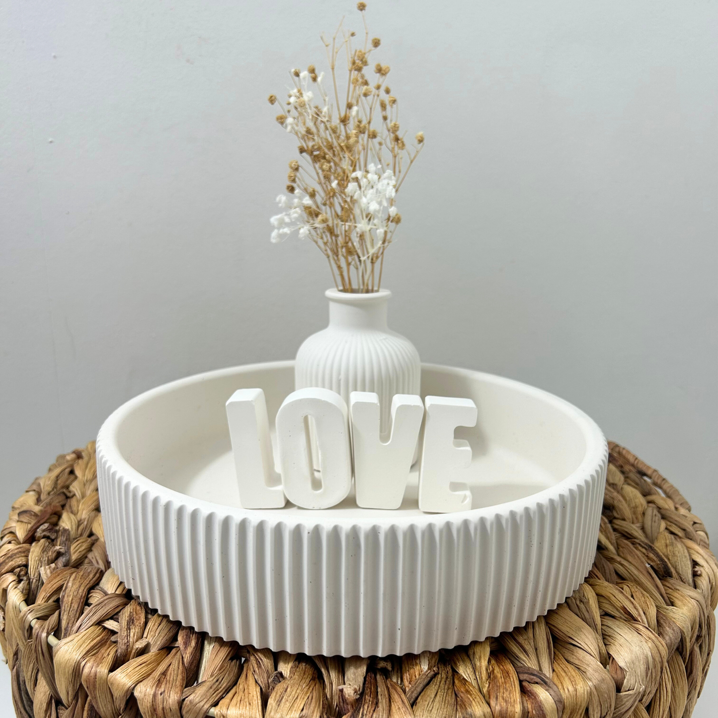 Decorative setup with a white vase and 'LOVE' letters on a textured surface.