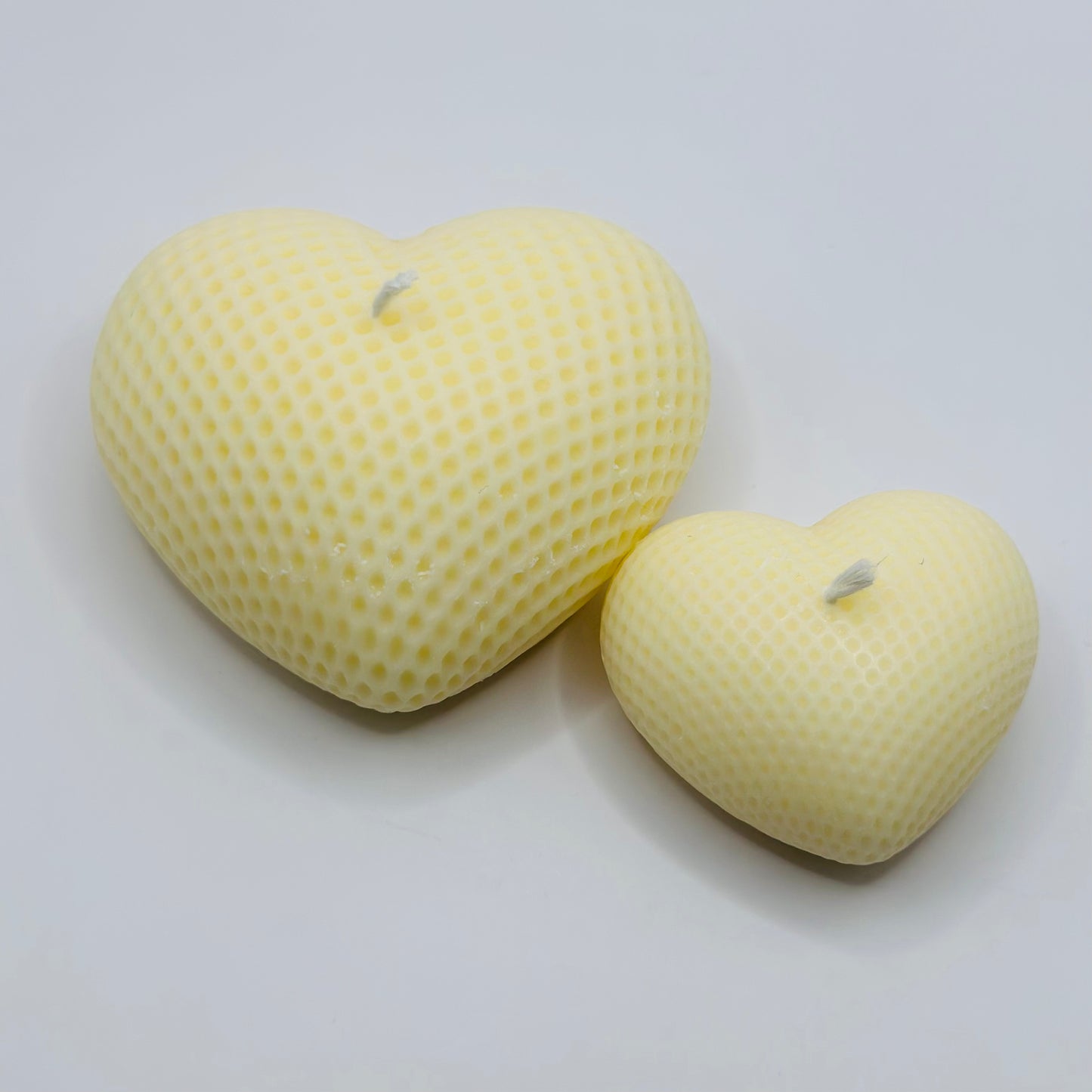 Two heart-shaped yellow candles on a light gray background