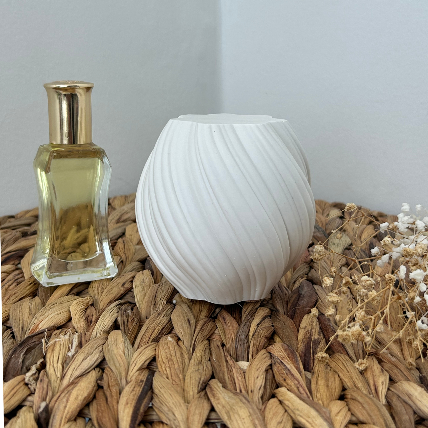 Perfume bottle and white twirl art on a woven surface with dried plants