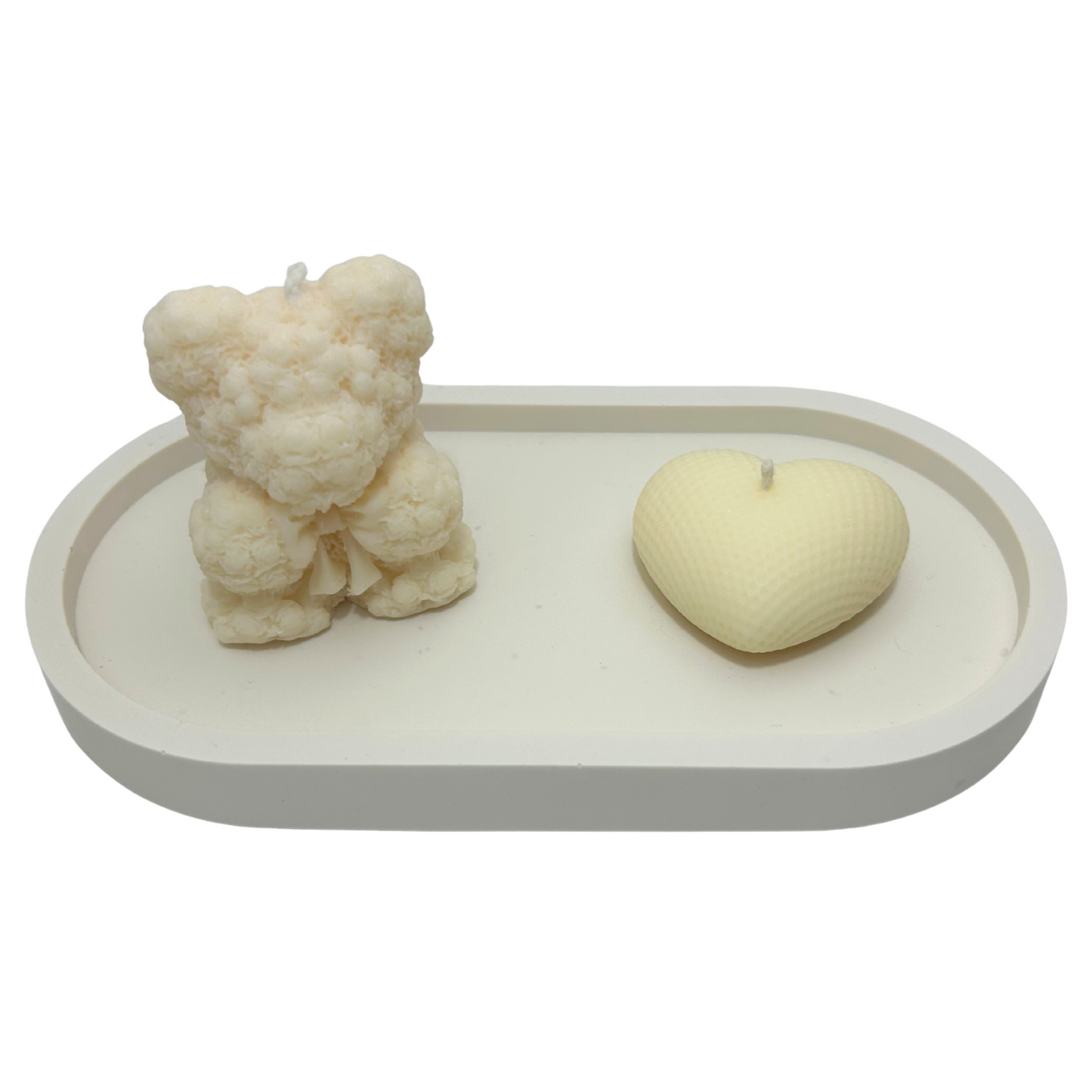 Two candles, one shaped like a bear and the other like a heart, on a white tray with a white background.