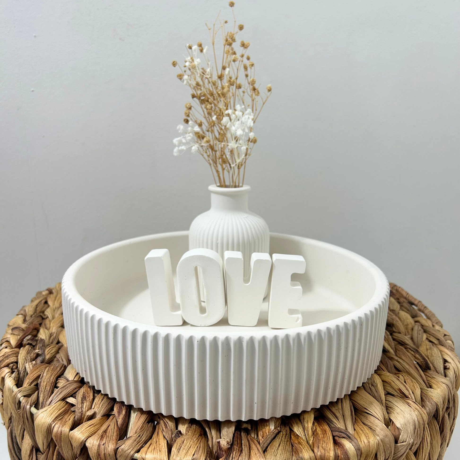 Decorative setup with a white vase and 'LOVE' letters on a textured surface.